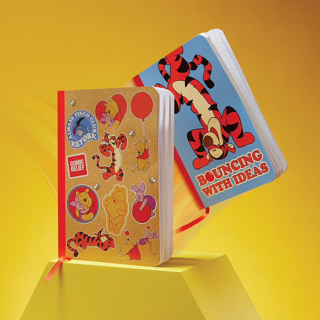 Two Winnie the Pooh–themed notebooks displayed against a bright yellow background. One notebook has a kraft-style cover decorated with colourful character stickers of Pooh, Tigger, and Piglet. The other notebook features a blue cover with a large illustration of Tigger bouncing and the text “Bouncing With Ideas.”